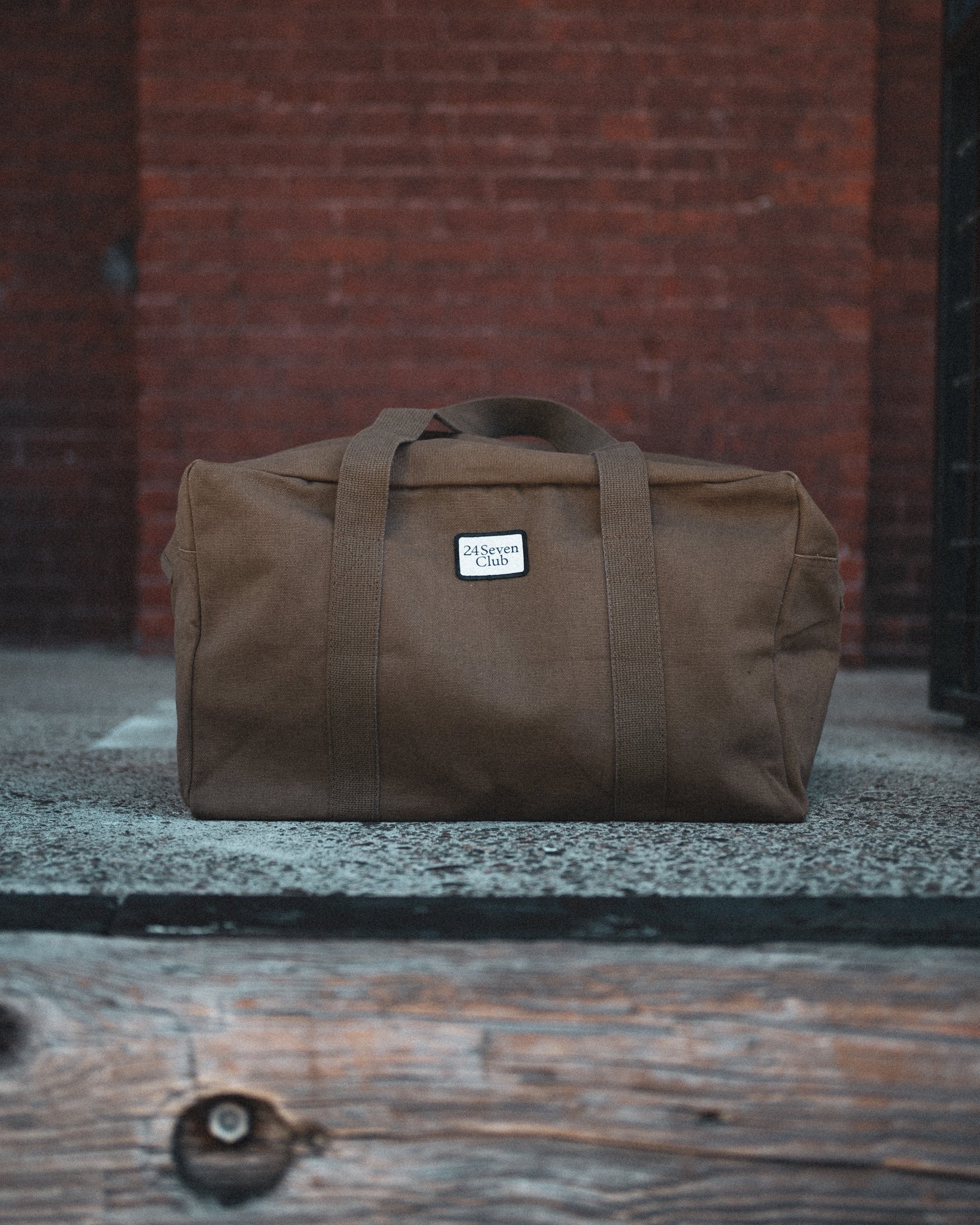 Brown canvas duffle bag with 24 seven club logo on a patch