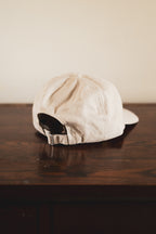 Cream cap with '24 Seven Club' logo on a wooden surface