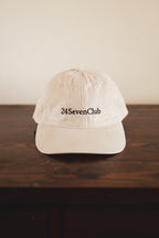 Cream cap with '24 Seven Club' logo on a wooden surface