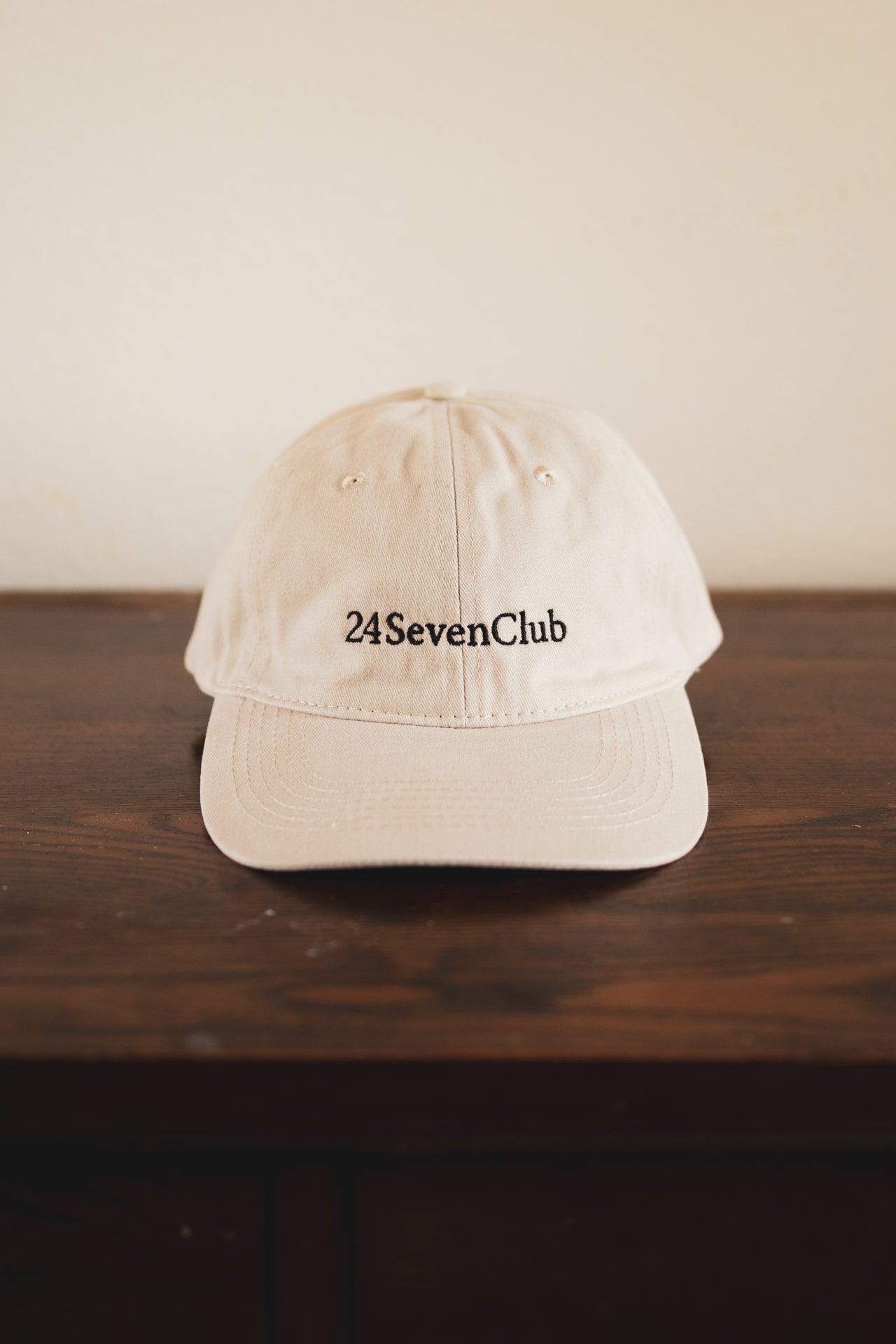 Cream cap with '24 Seven Club' logo on a wooden surface