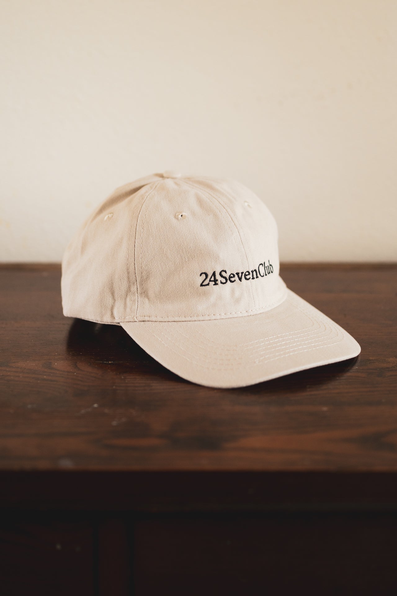 Cream cap with '24 Seven Club' logo on a wooden surface
