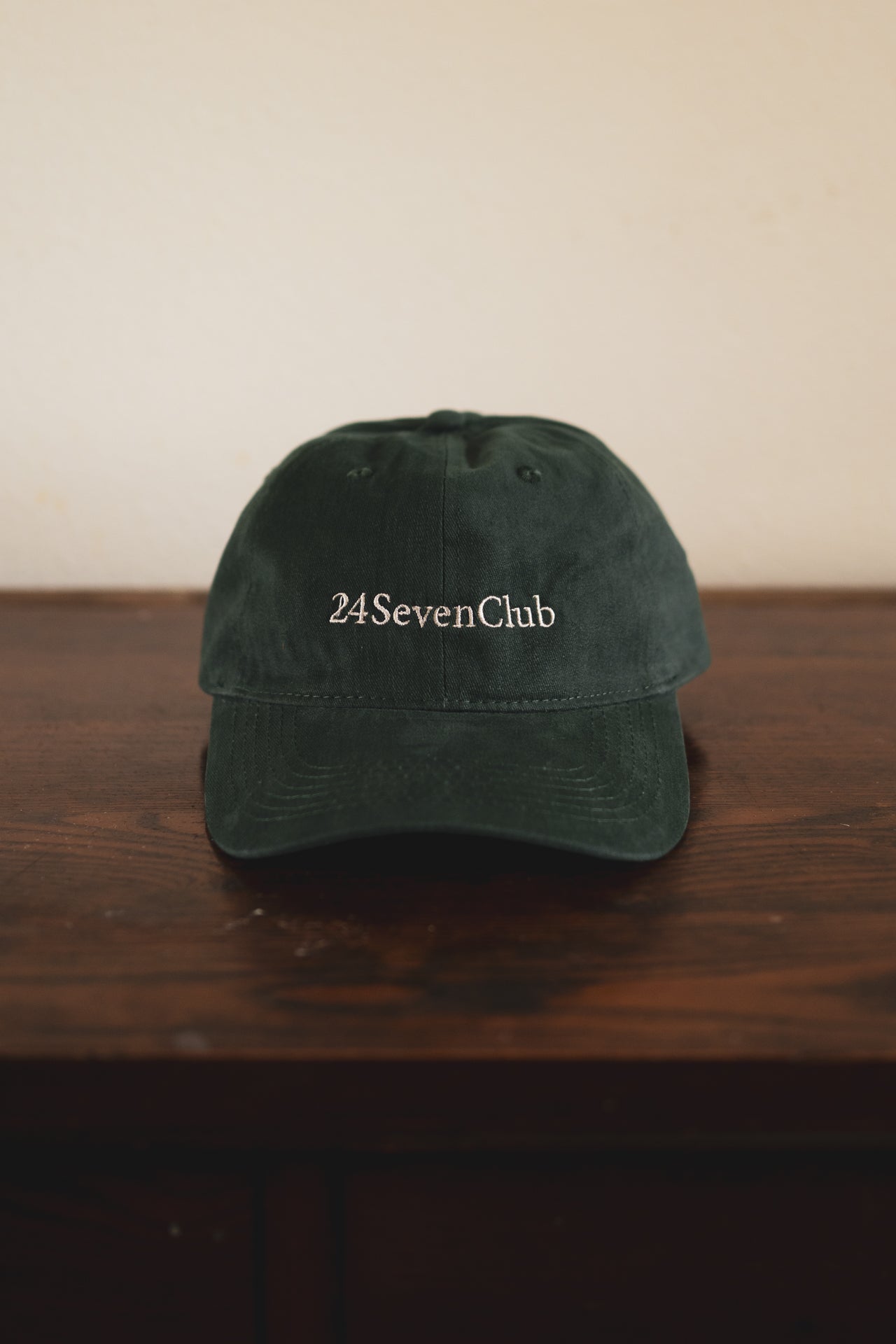Green cap with '24SevenClub' text on a wooden surface