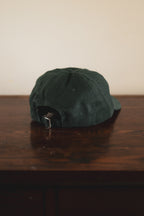 Green 24 seven club cap on a wooden surface with a plain background