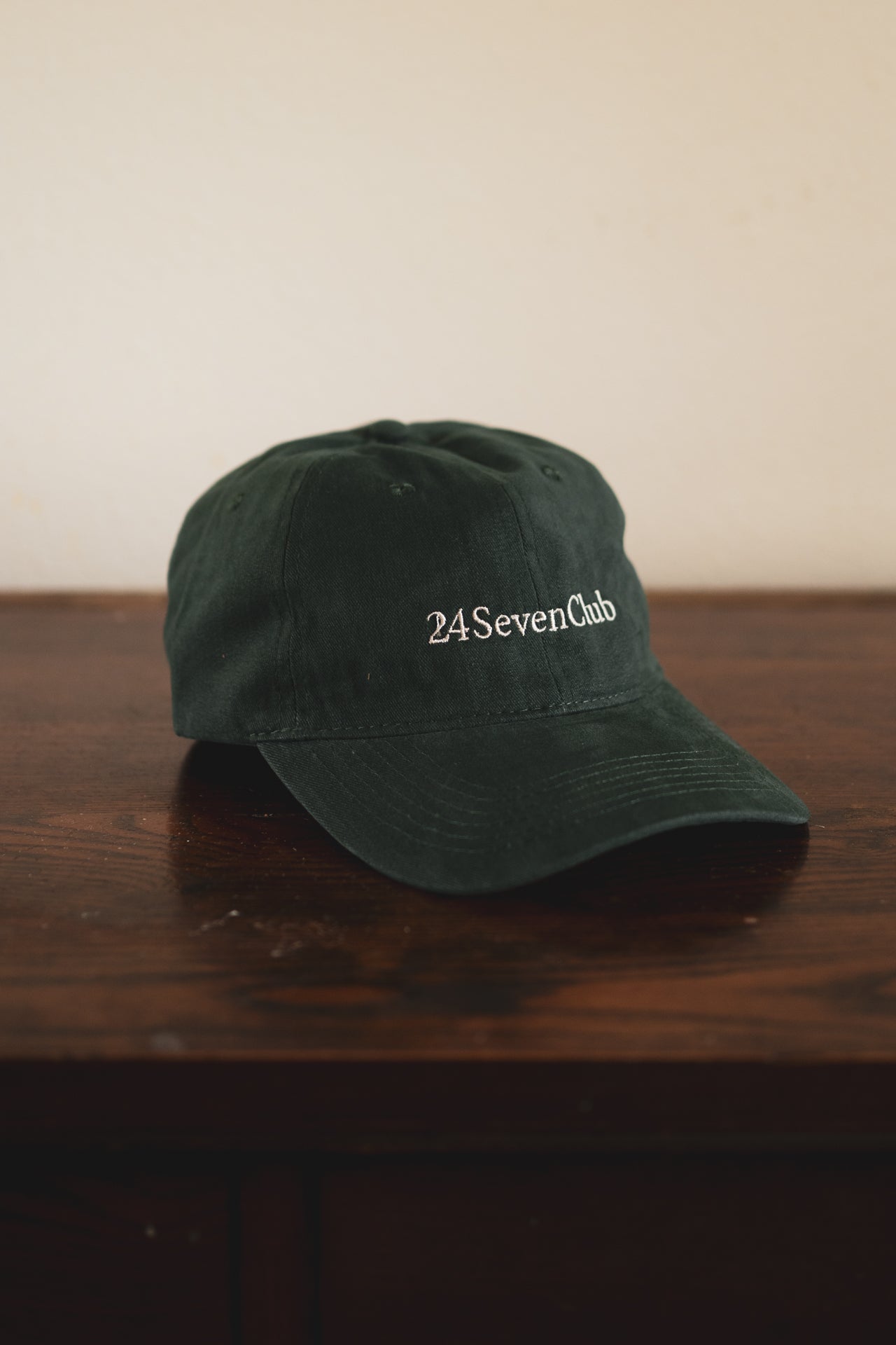 Green cap with '24SevenClub' text on a wooden surface