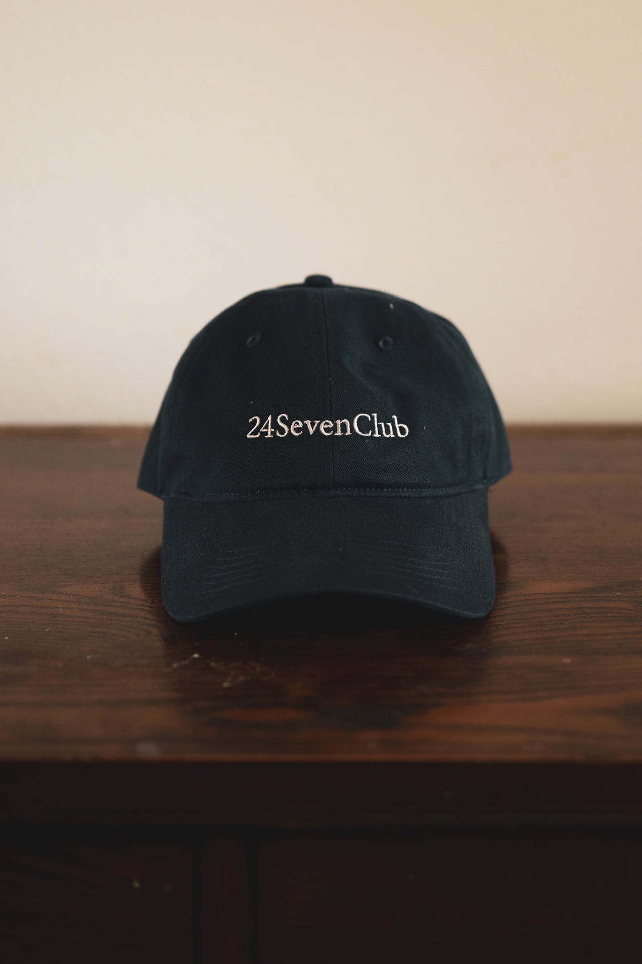 Navy cap with '24 Seven Club' embroidered logo on a wooden surface