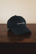 Navy cap with '24 Seven Club' embroidered logo on a wooden surface
